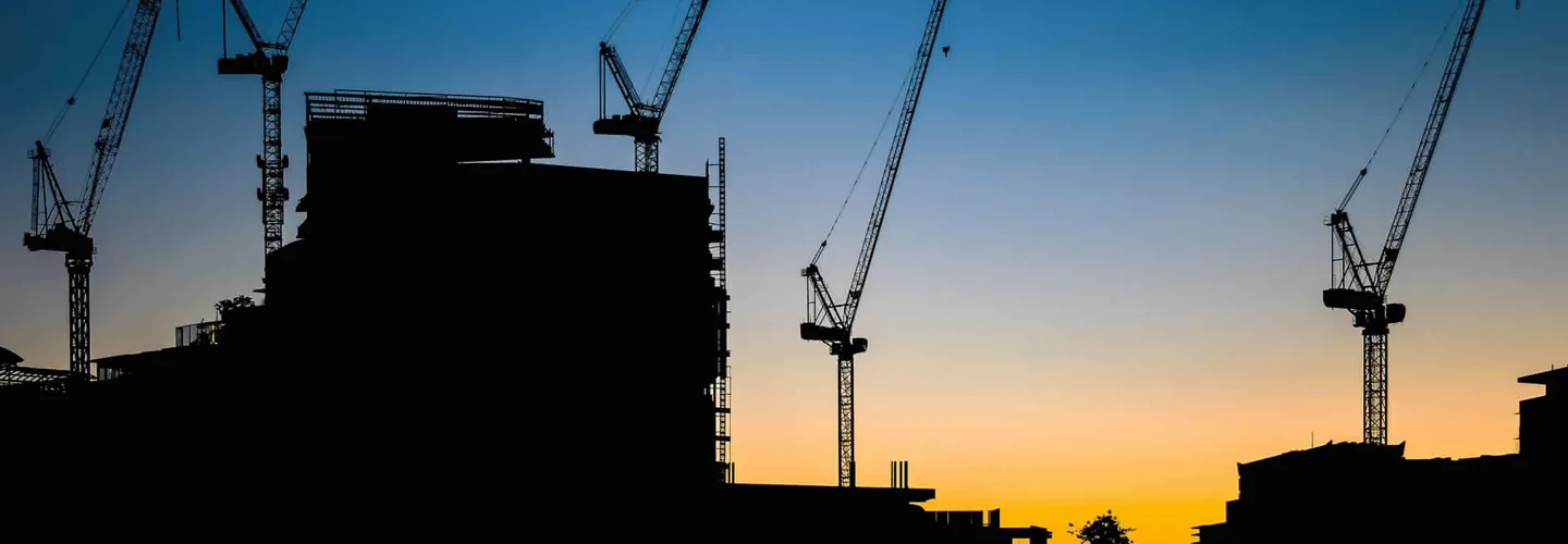 Baukräne vor Abendhimmel über einer Großbaustelle
